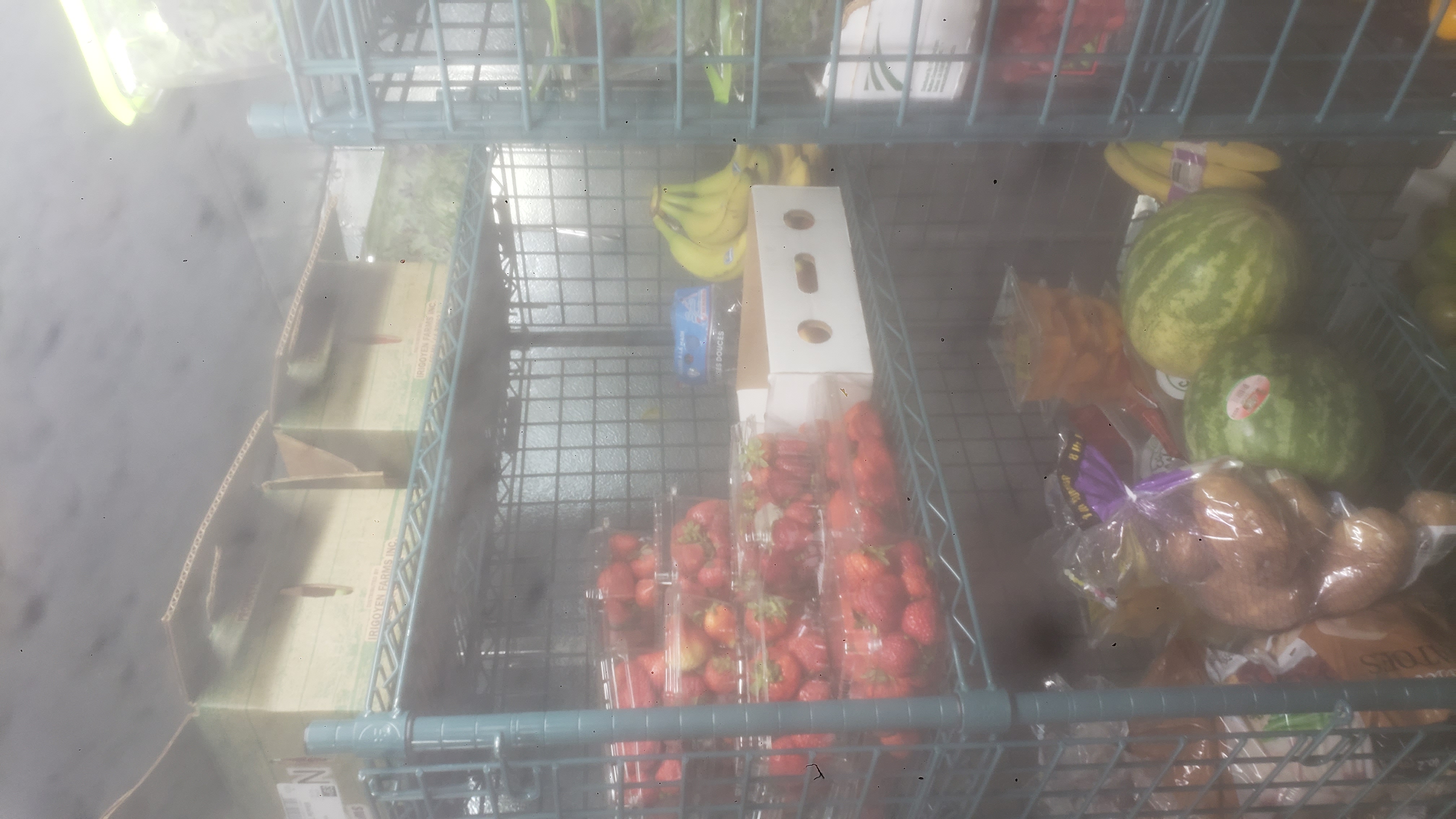 Assorted produce in bags, crate, and trays on shelves of a cage shelf.