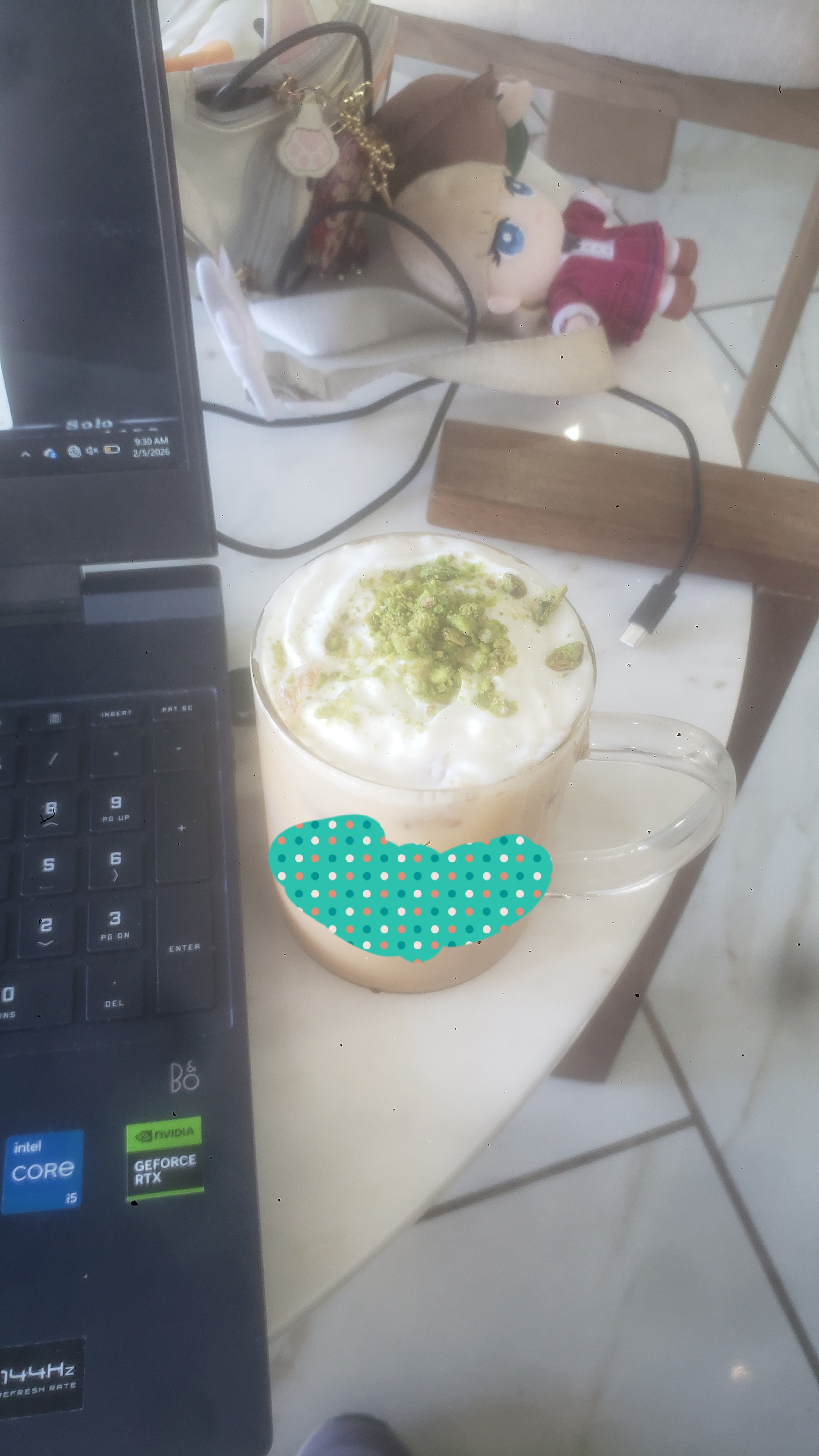 Glass cup of coffee next to cat fanny and laptop.