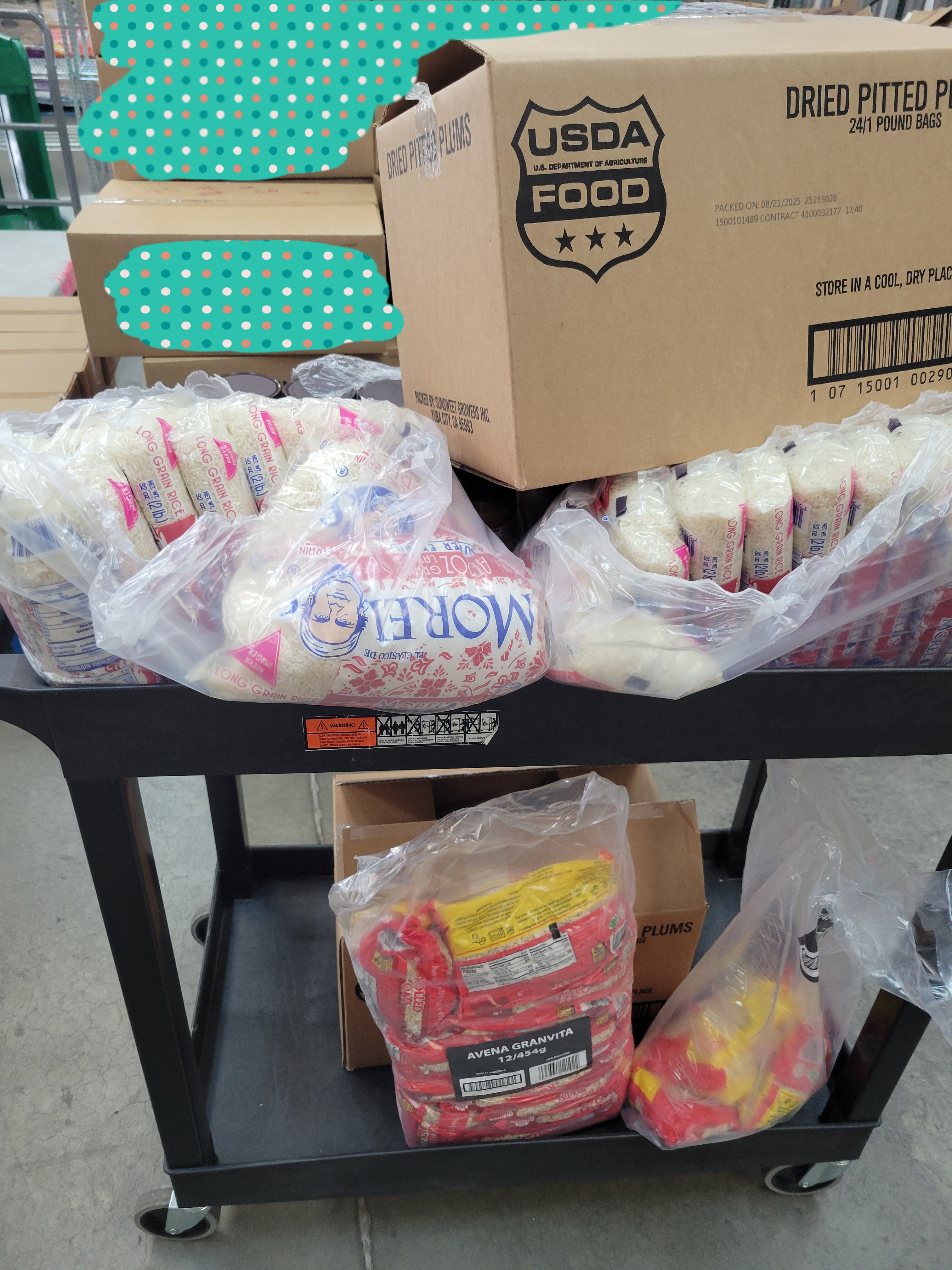 Box of pitted plums and bags of rice on the top of a shelf cart with another box of pitted plums and bags of oatmeal on the bottom.
