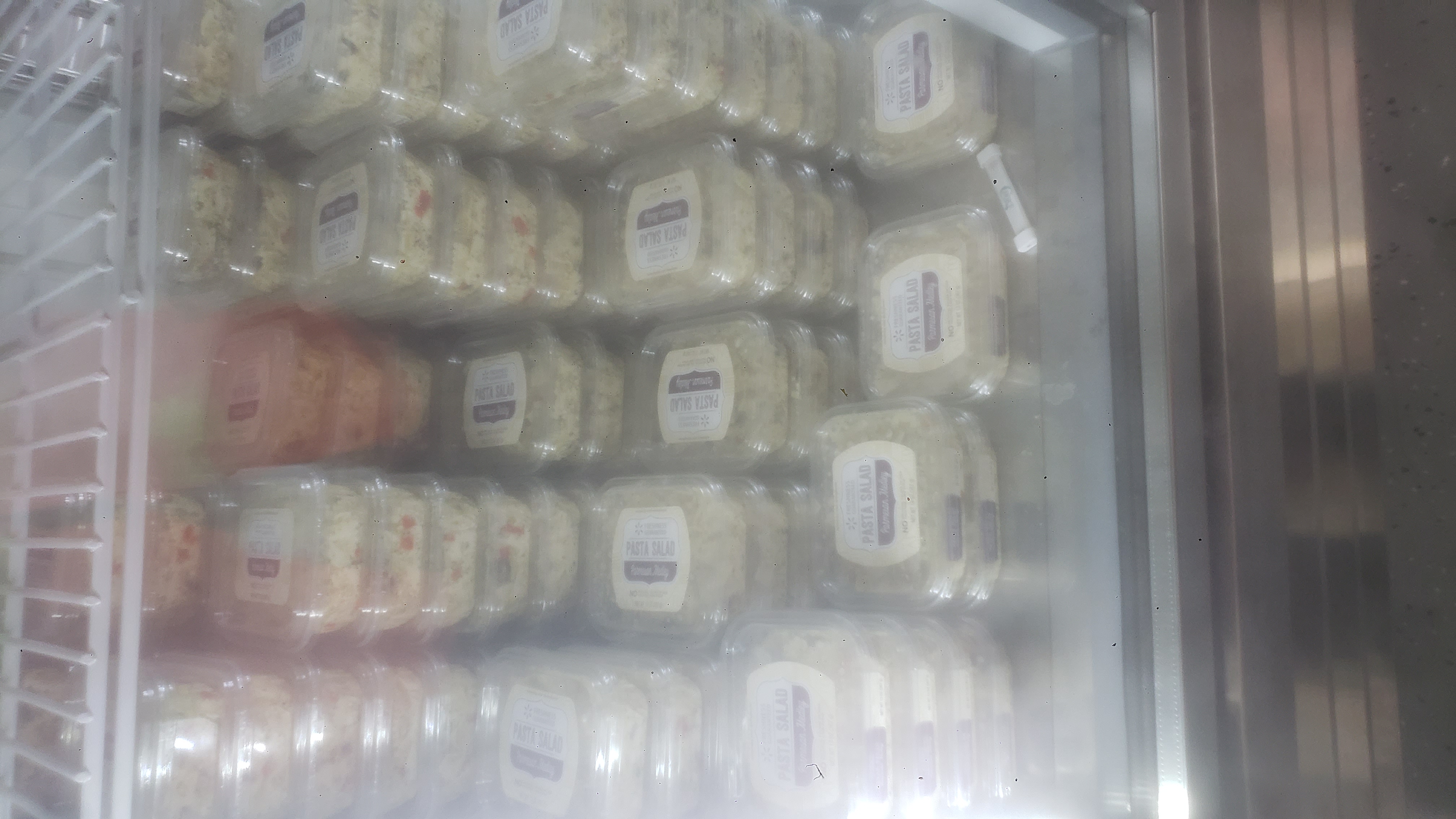 Containers of pasta salad stacked on each other in a fridge.