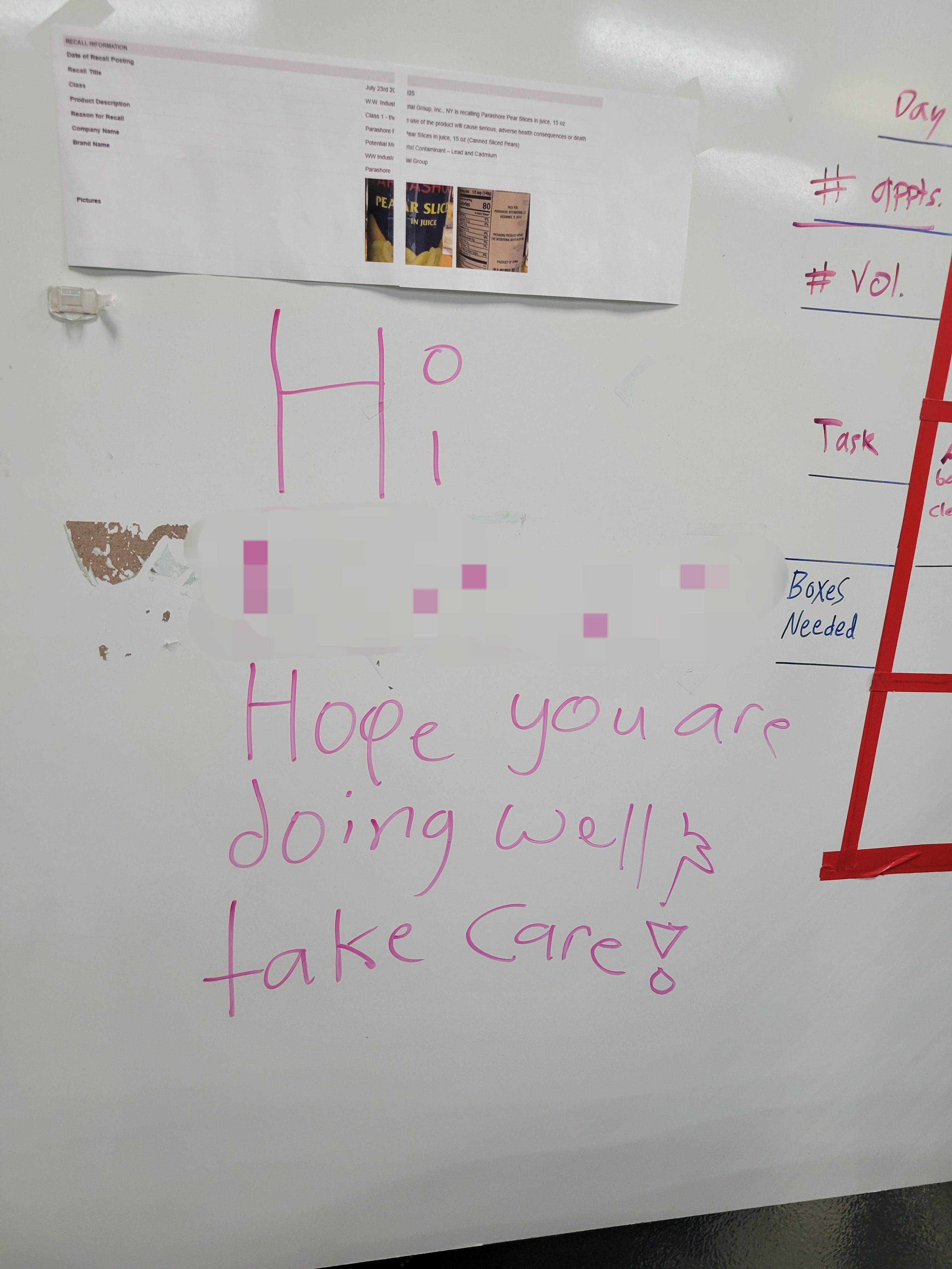 Piece of paper listing a product recall, a greeting to a fellow volunteer in dry erase marker under it on a dry erase board.