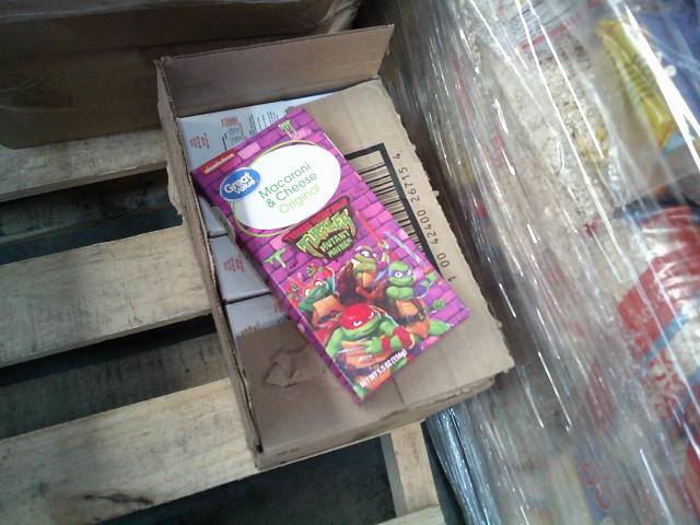 Box of Teenage Mutant Ninja Turtles themed macaroni and cheese on top of cardboard box.