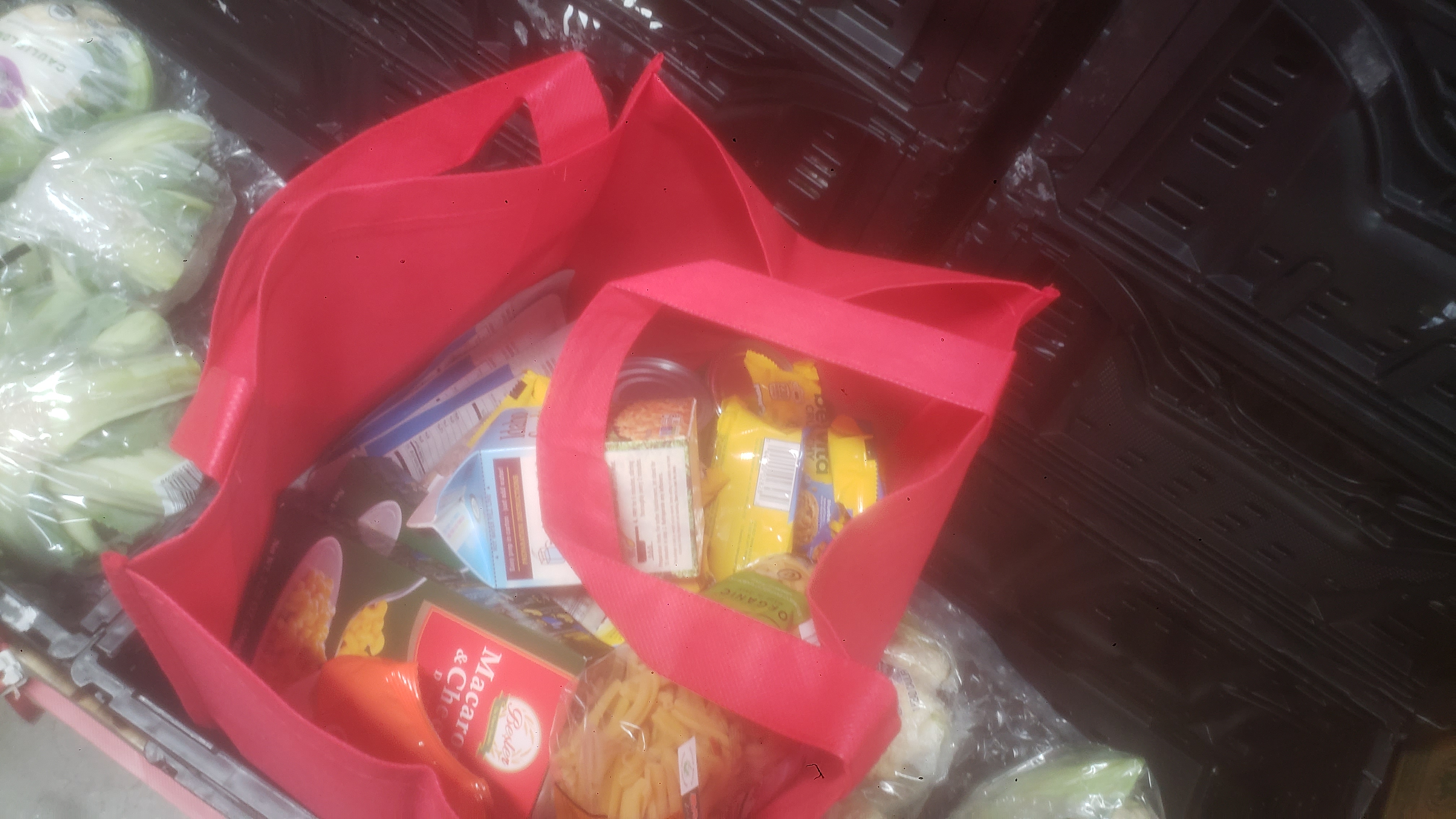 Food filled tote bag on top of crates of lettuce.