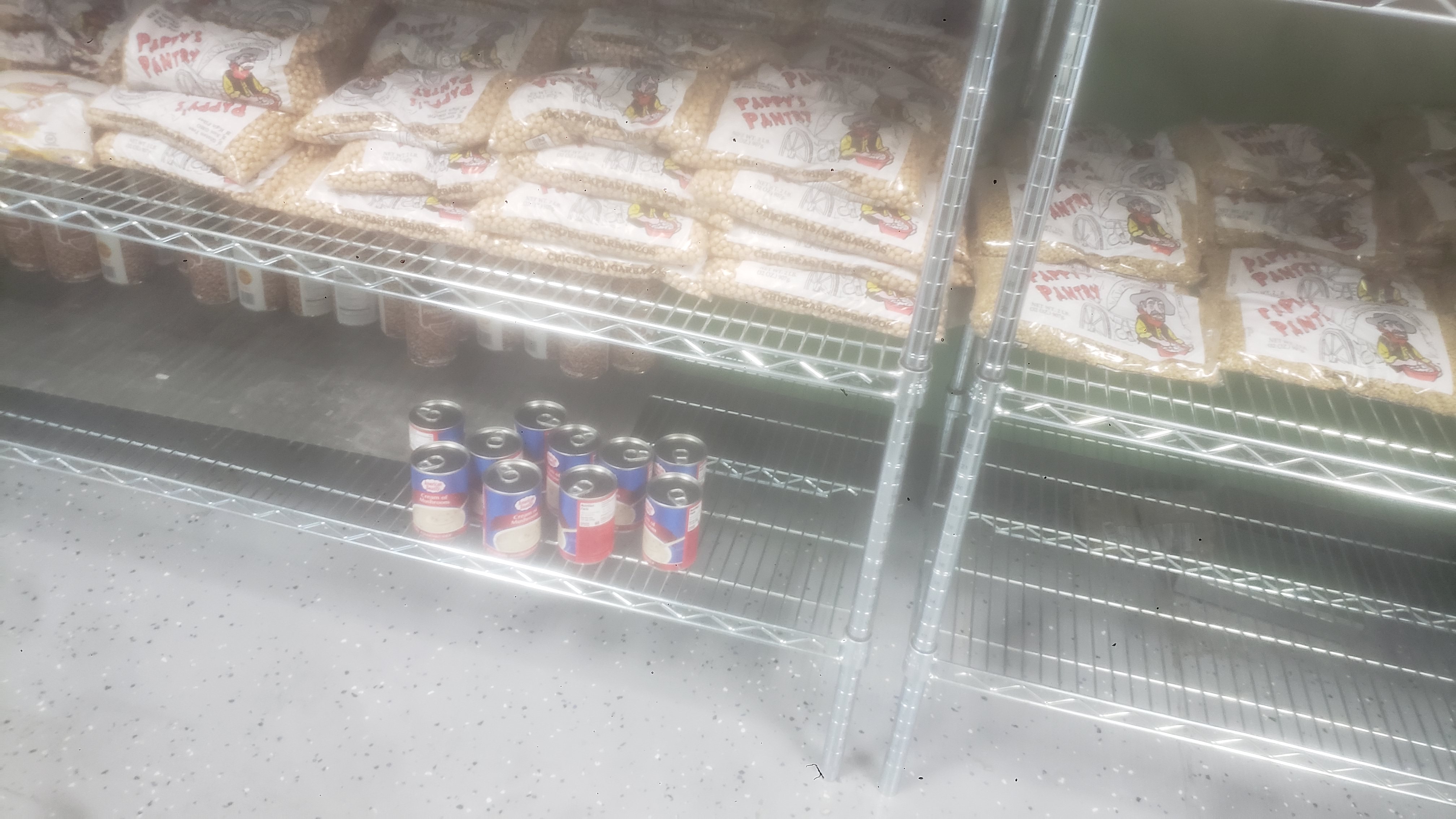 Bags of chickpeas, cans of cream of mushrooms, cans of pinto bean. and bags of lentils on a shelf.
