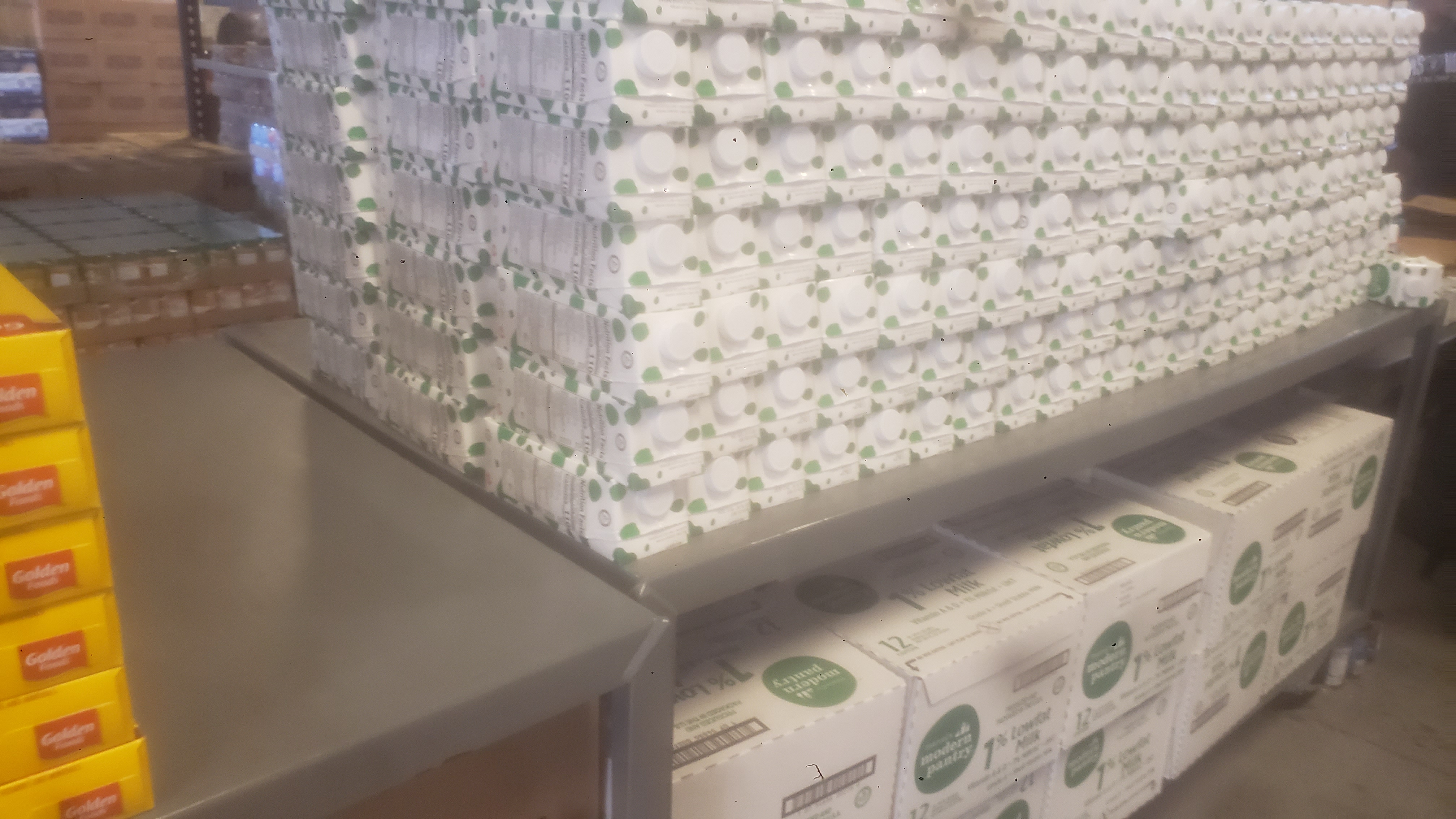 Rows of boxed milk on a metal table next to boxes of cereal.