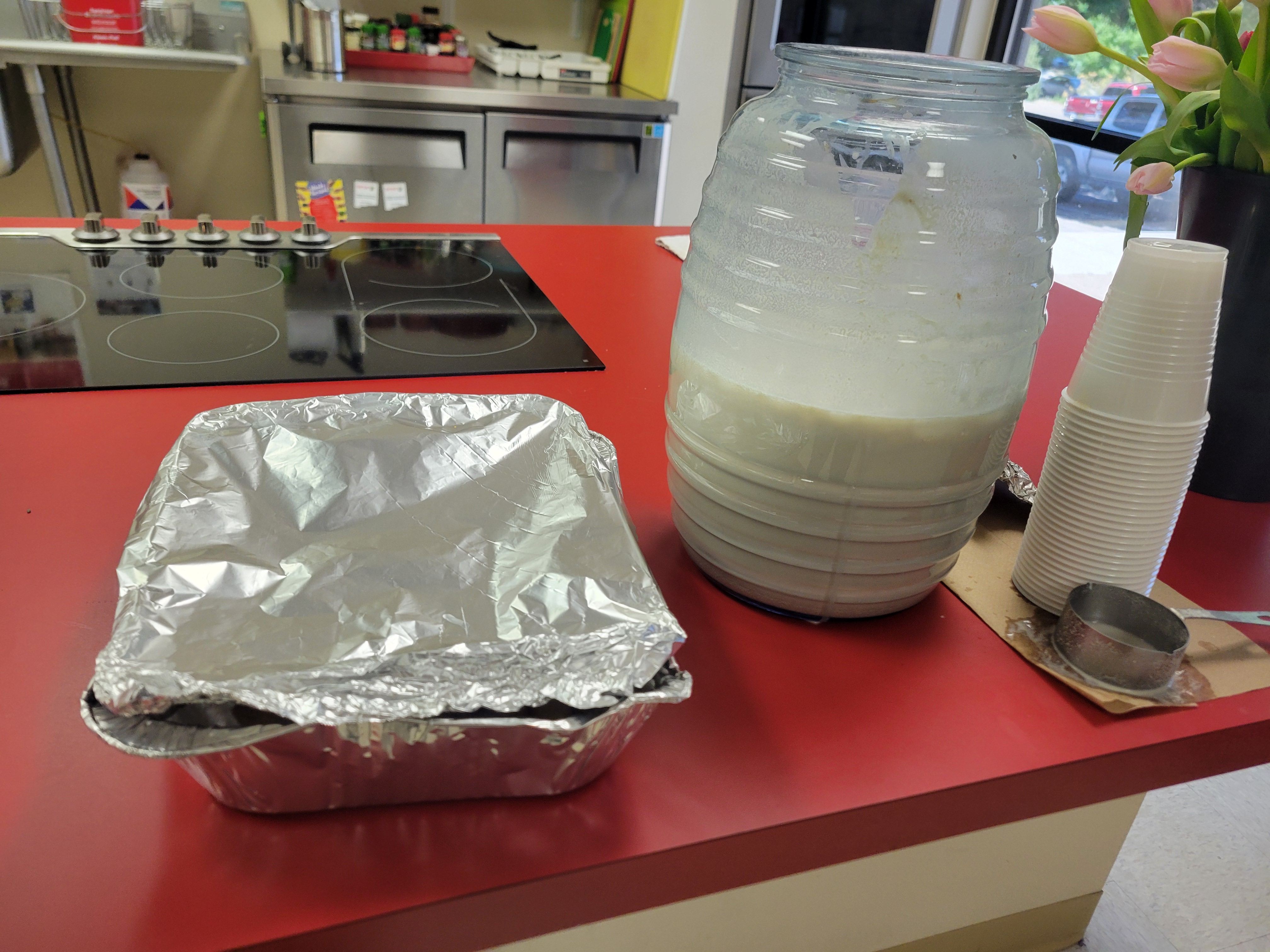 Large plastic jar/vitrolero full of horchata and tin foil pan full of food.