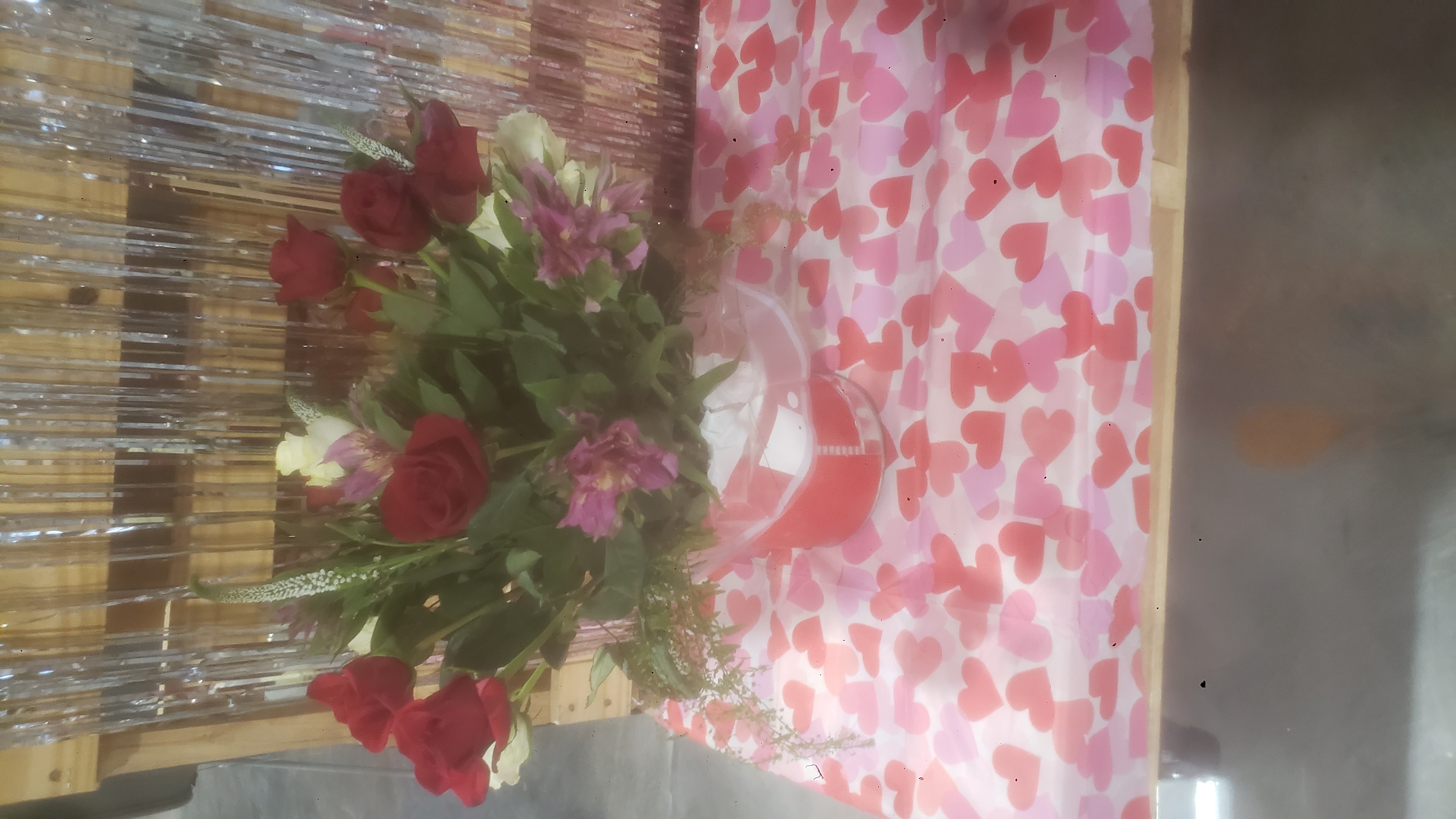 A floral arrangement featuring red roses, pink flowers, and white flowers on a heart table runner.