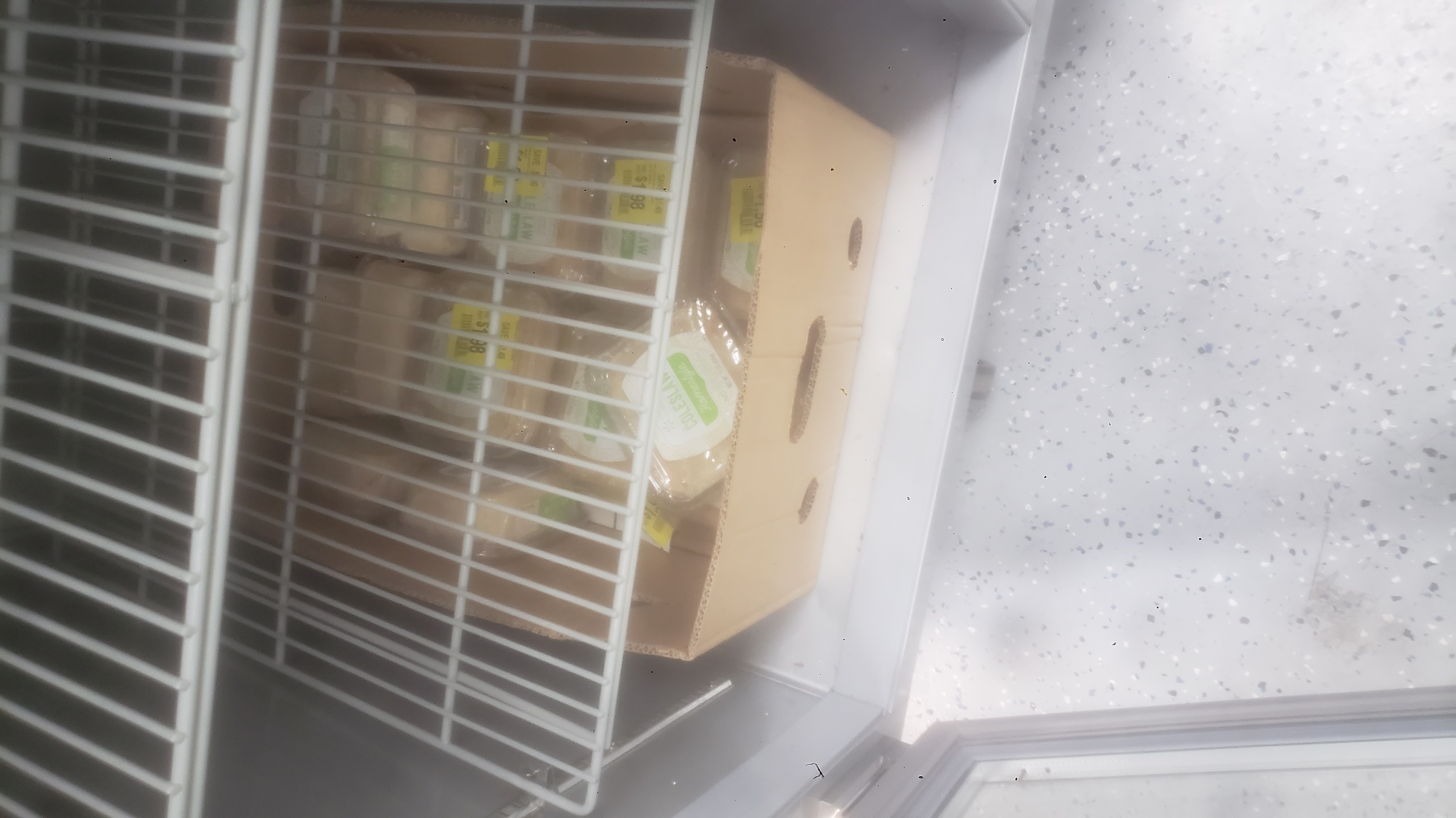 Banana box full of containers of coleslaw in a fridge.