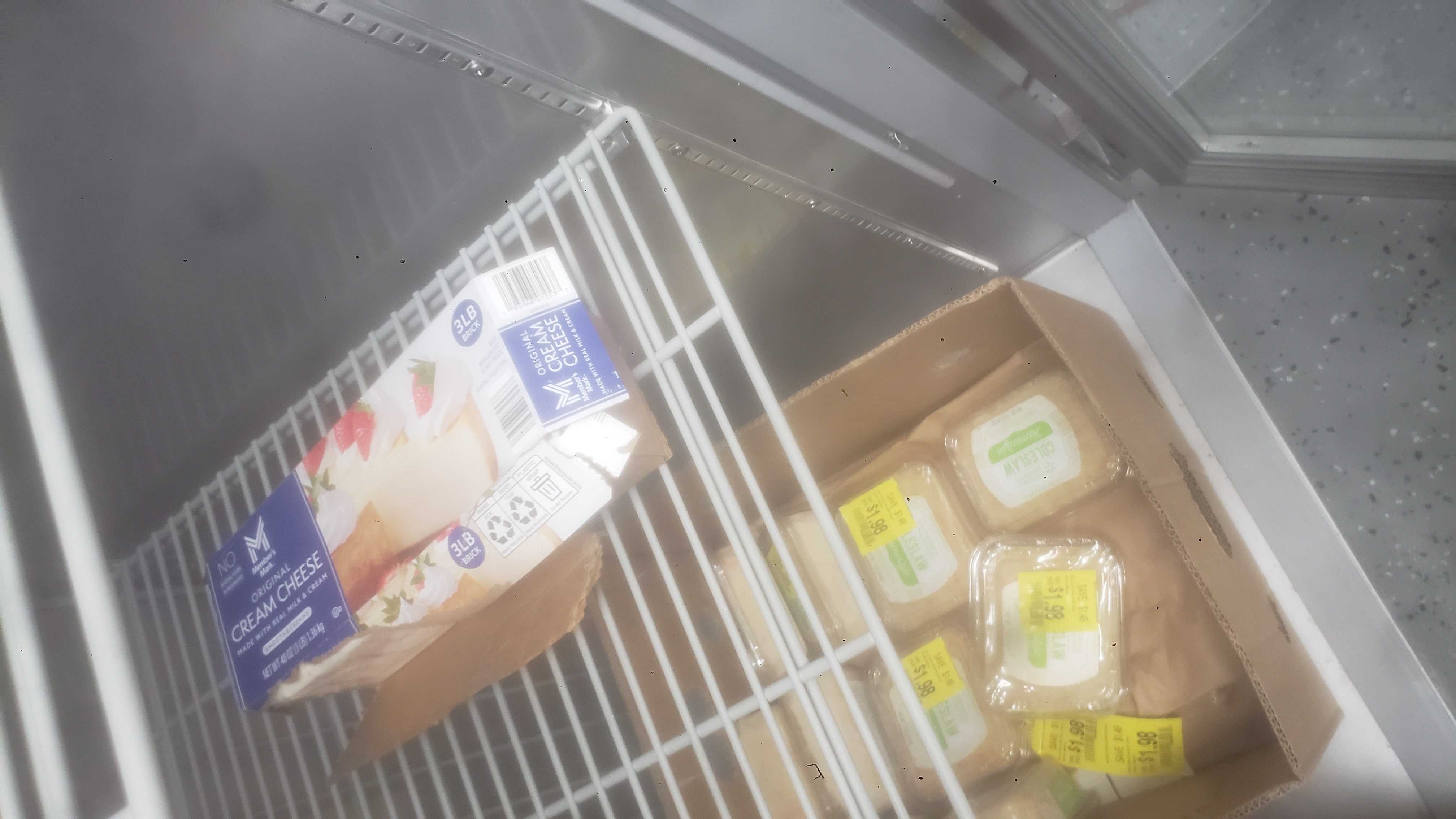 Box of cream cheese and containers of coleslaw in a fridge.