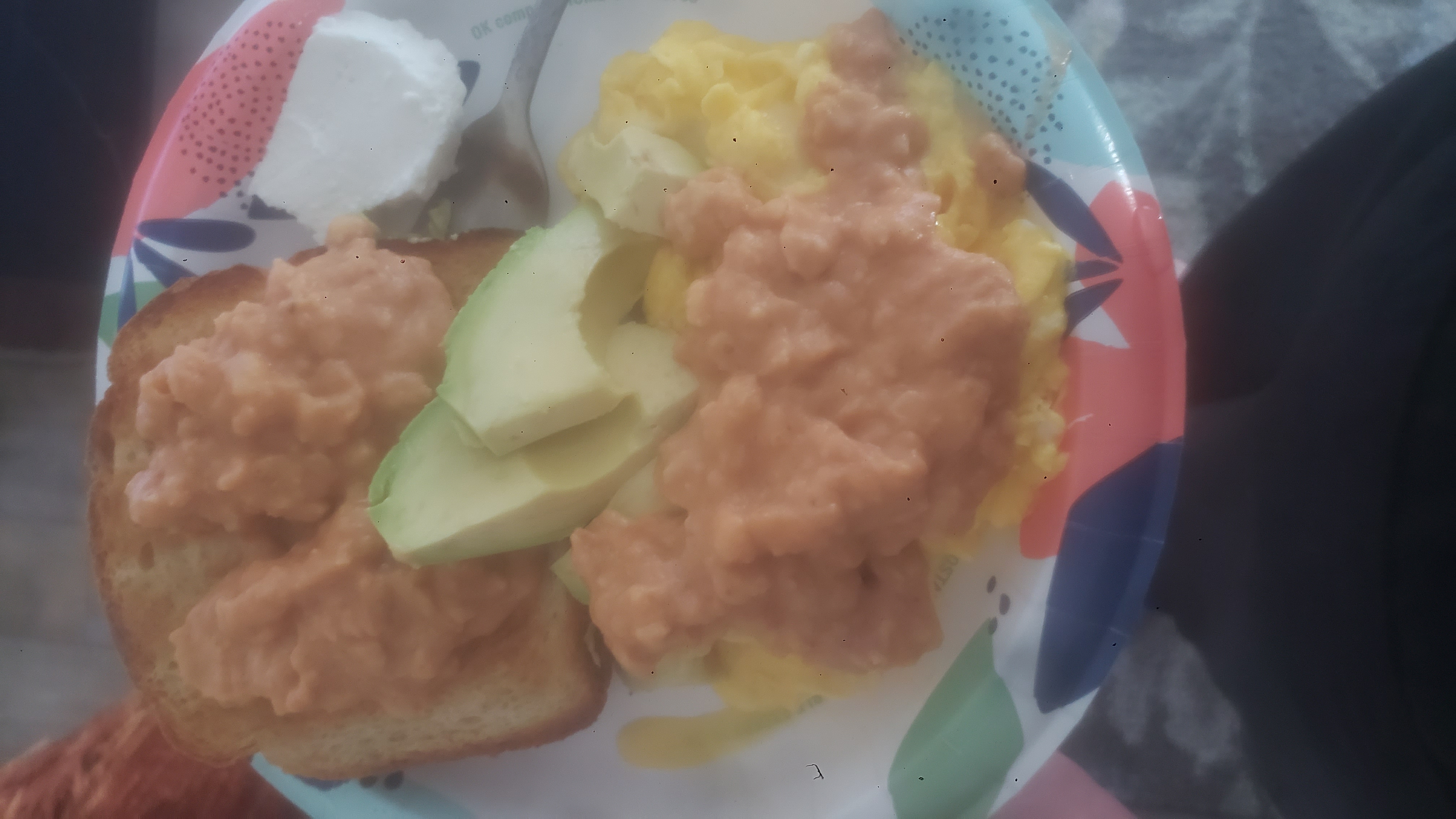 Eggs and toast topped with beans plus avocados on a paper plate.
