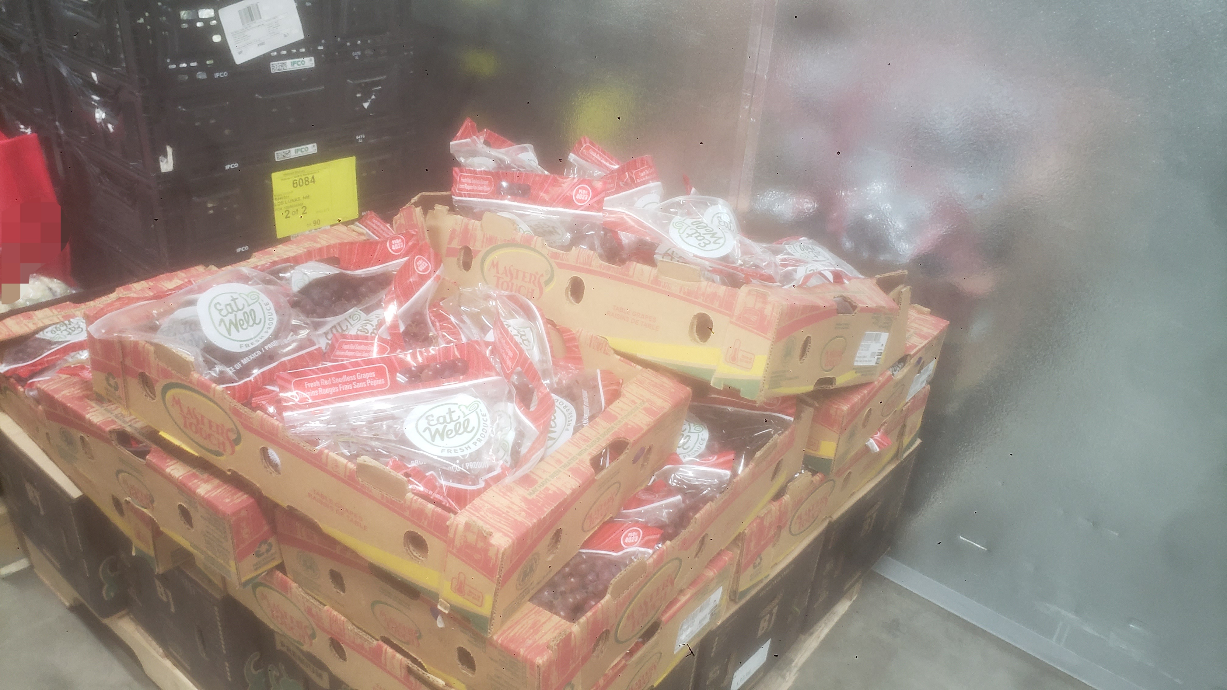 Bags of red grapes in trays on top of cardboard boxes.