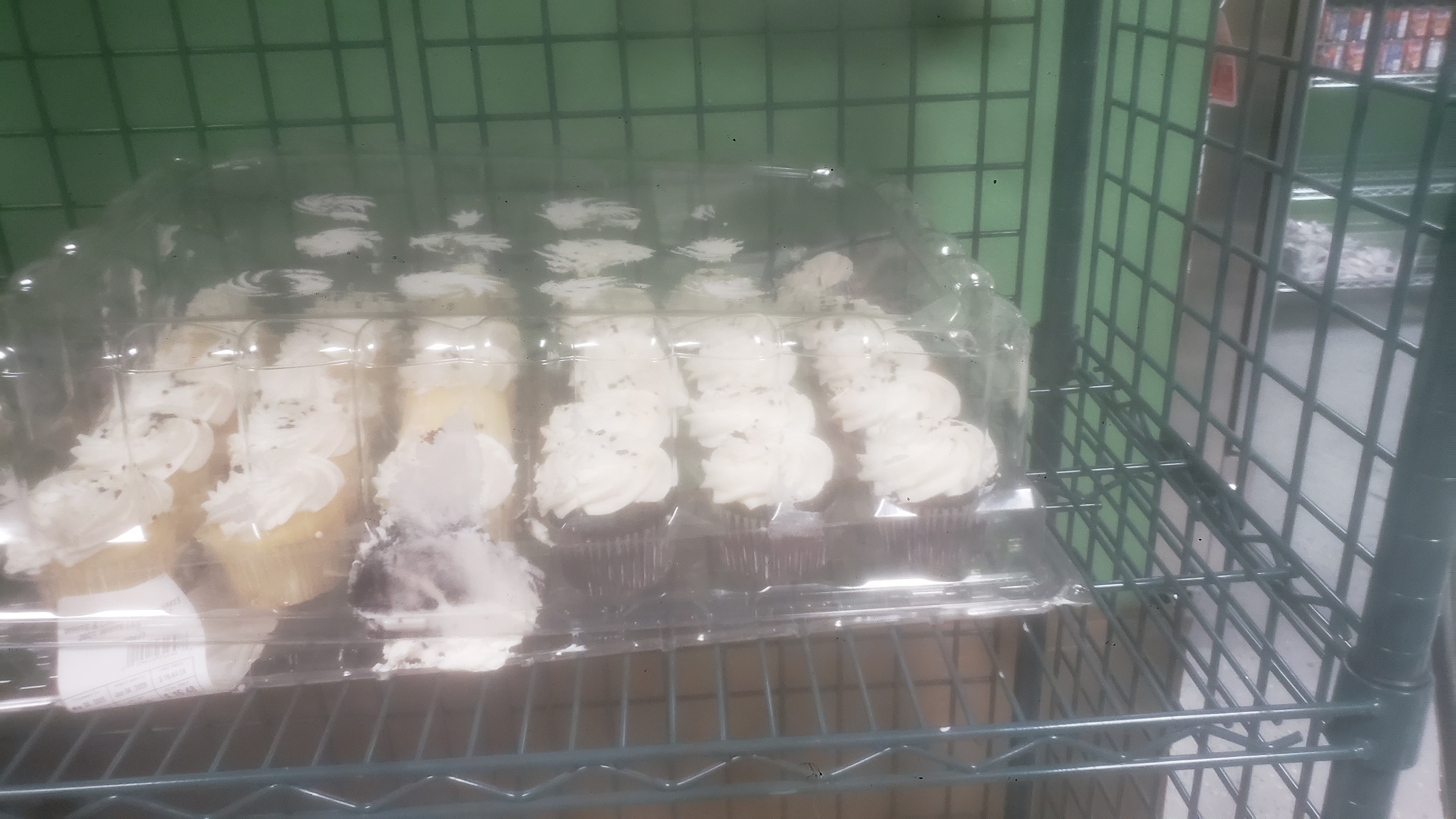 Vanilla and chocolate cupcakes with white frosting and sprinkles in a plasic container.