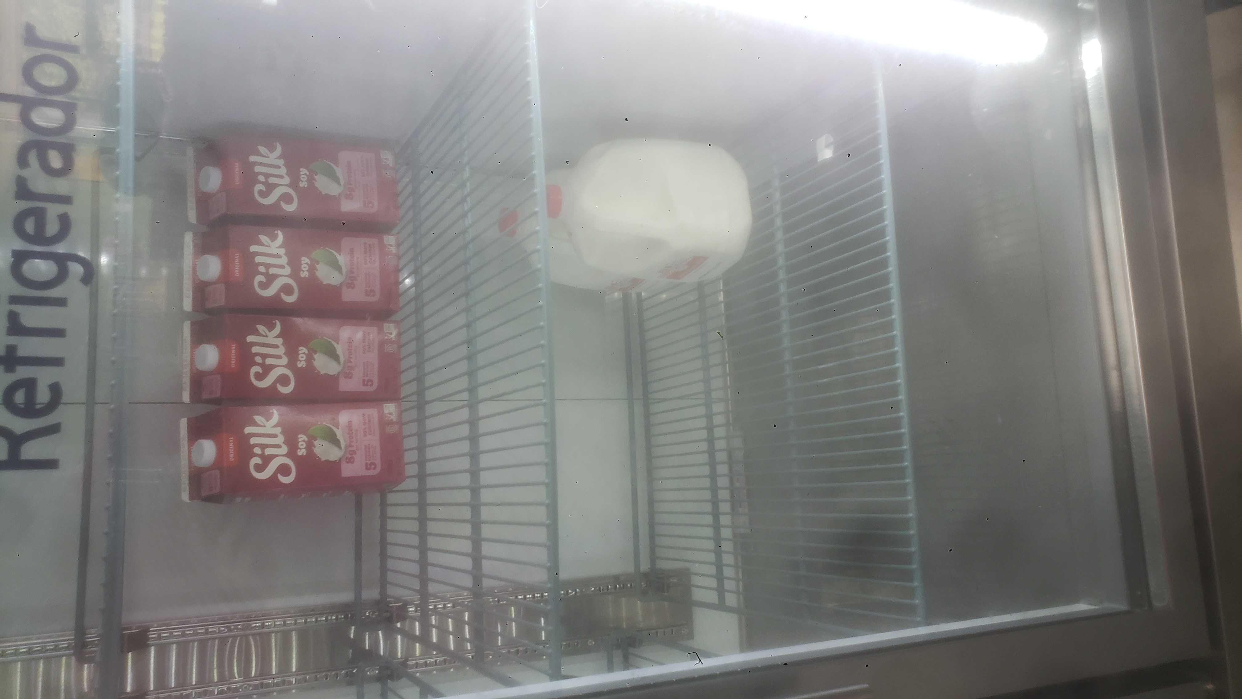 Cartons of soy milk and gallons of milk in a fridge.