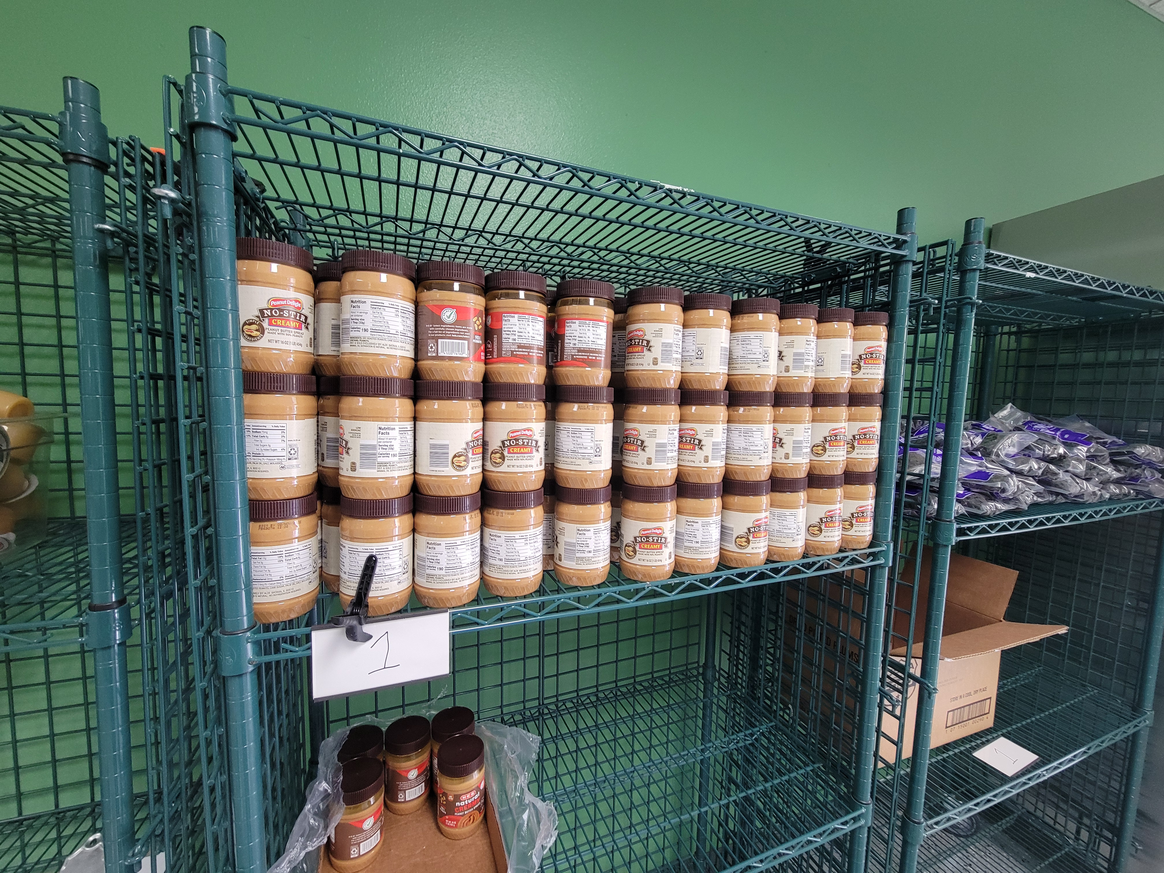 Jars of peanut butter on the top and second shelf of a shelf next to a shelf of bags of pitted plums.