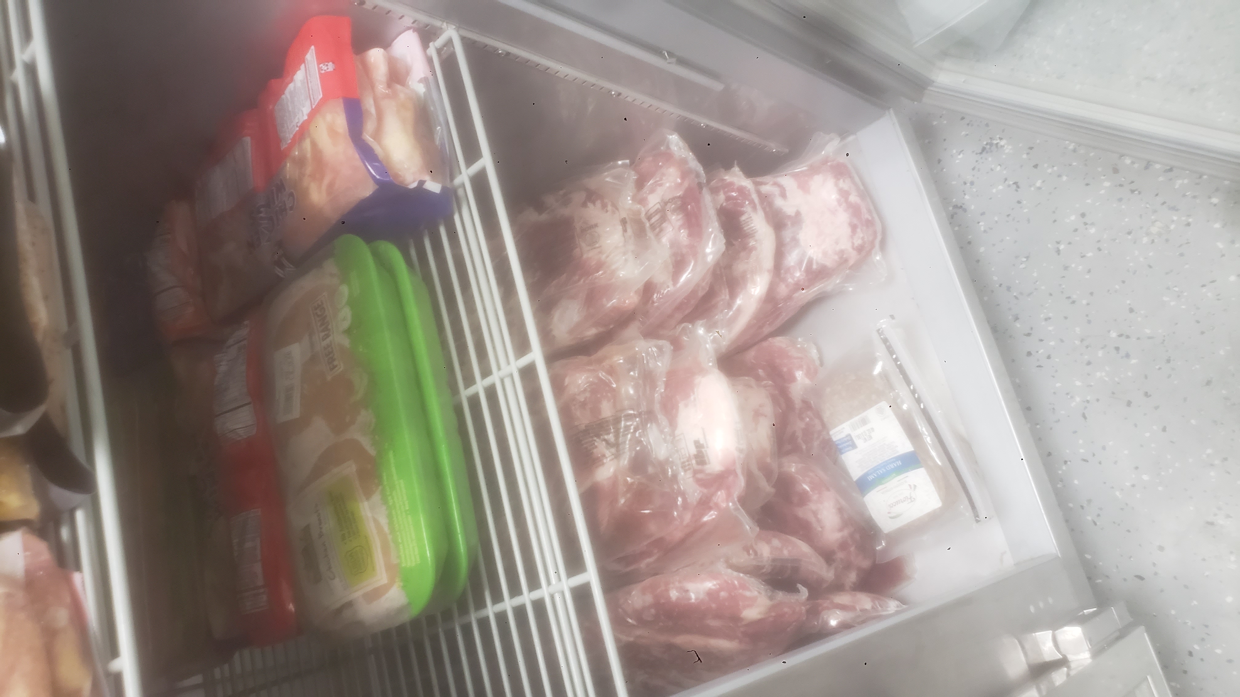 Assorted meats on shelves of a fridge.
