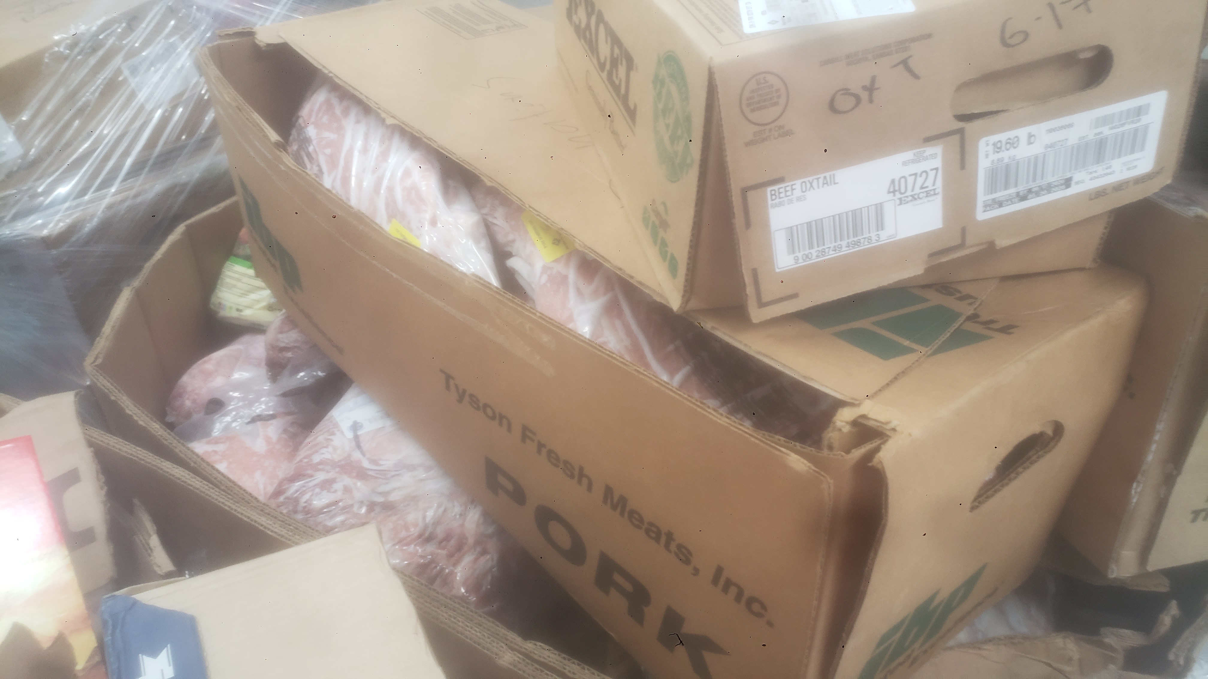 Assorted frozen items in cardboard boxes and container such as beef oxtail and pork.