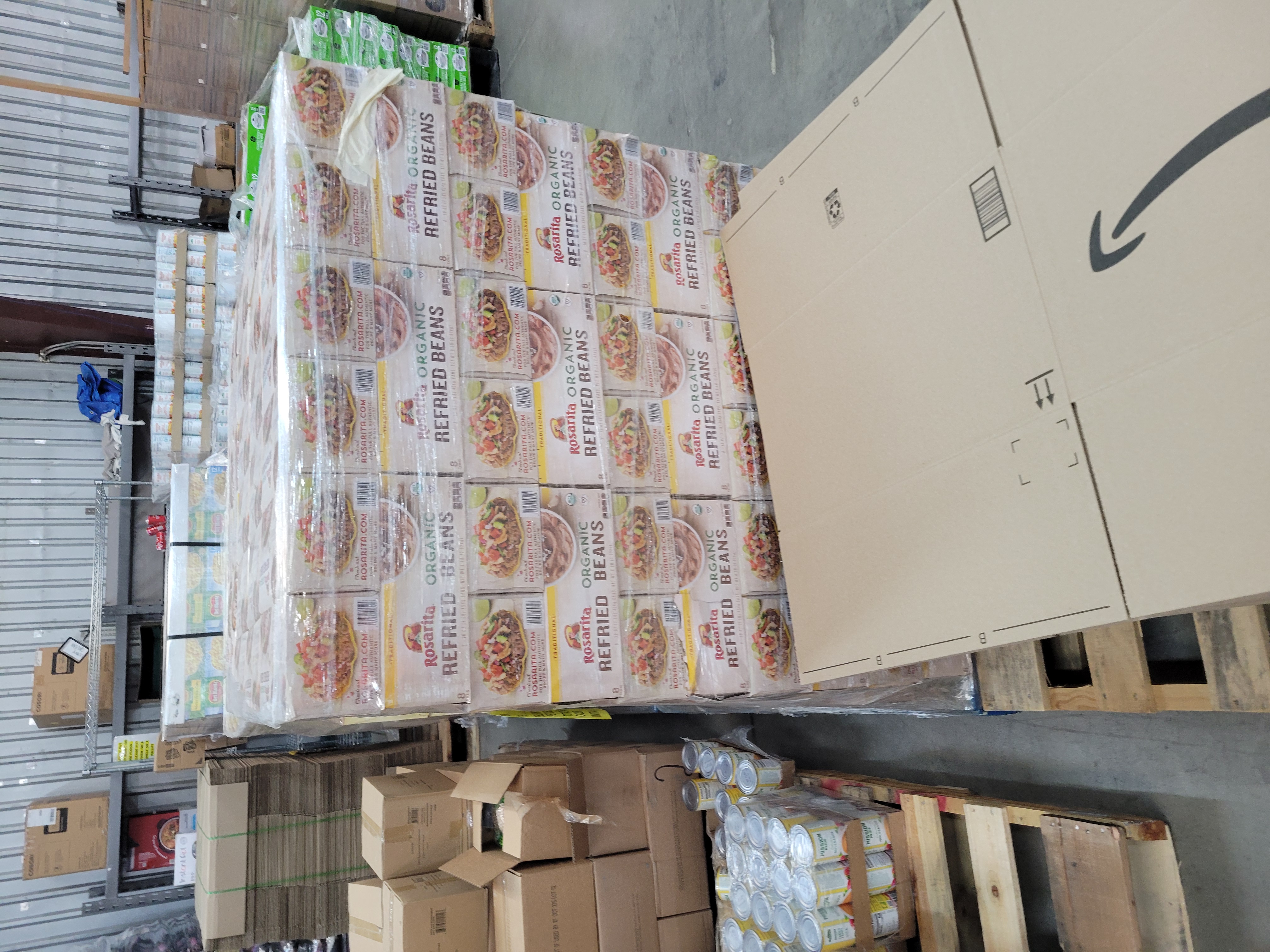Flatted amazon boxes on a pallet with a pallet of canned refried beans behind it.