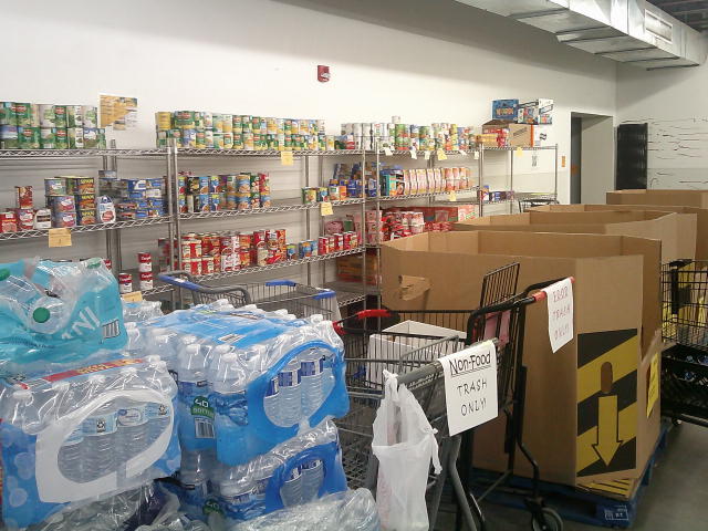 Pallets of water, cardboard containers and shopping carts with shelves of canned goods behind them. 