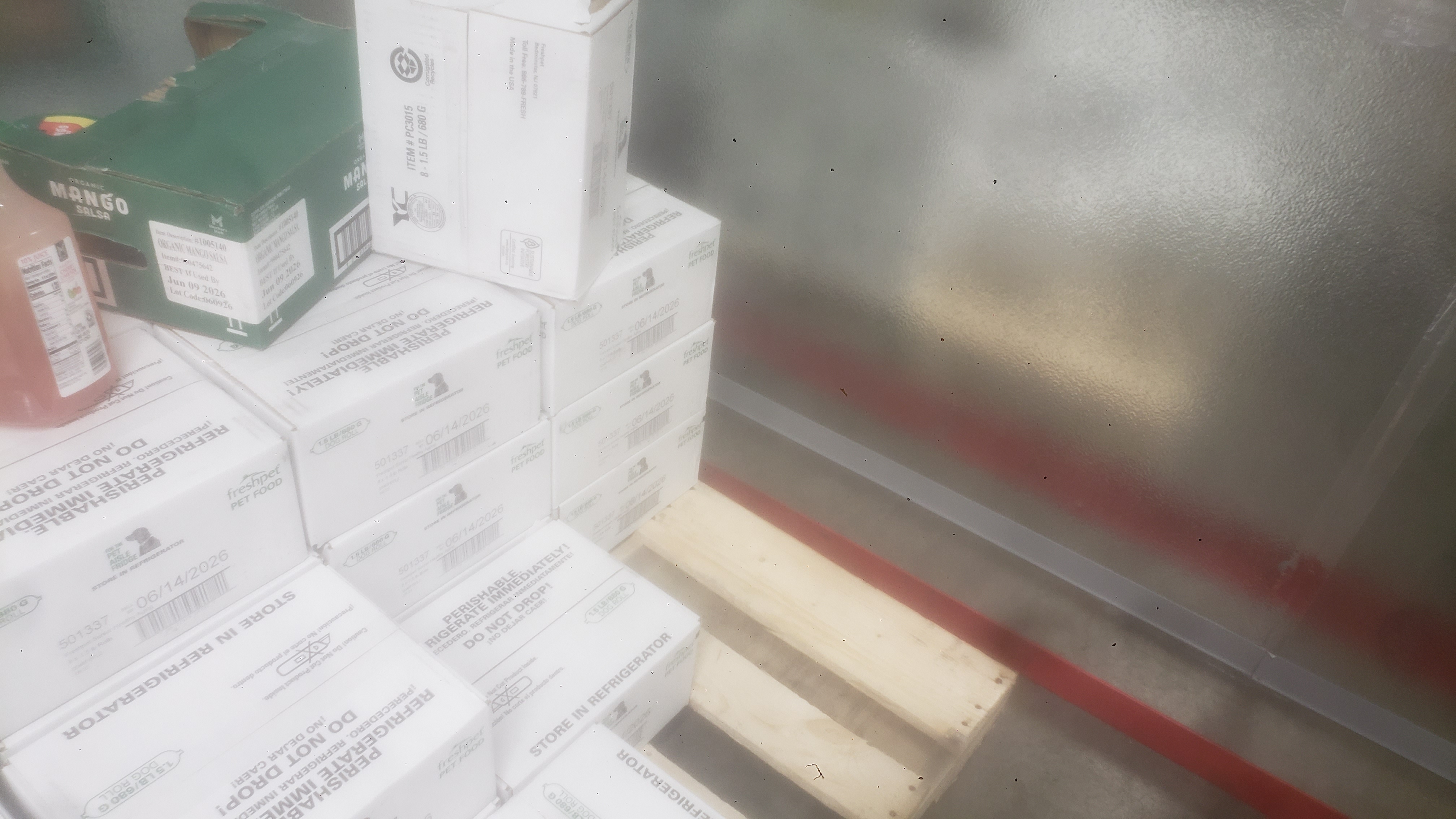 Bottles of cherry limeade and jars of mango salsa in a shipping tray on top of boxes of pet food.