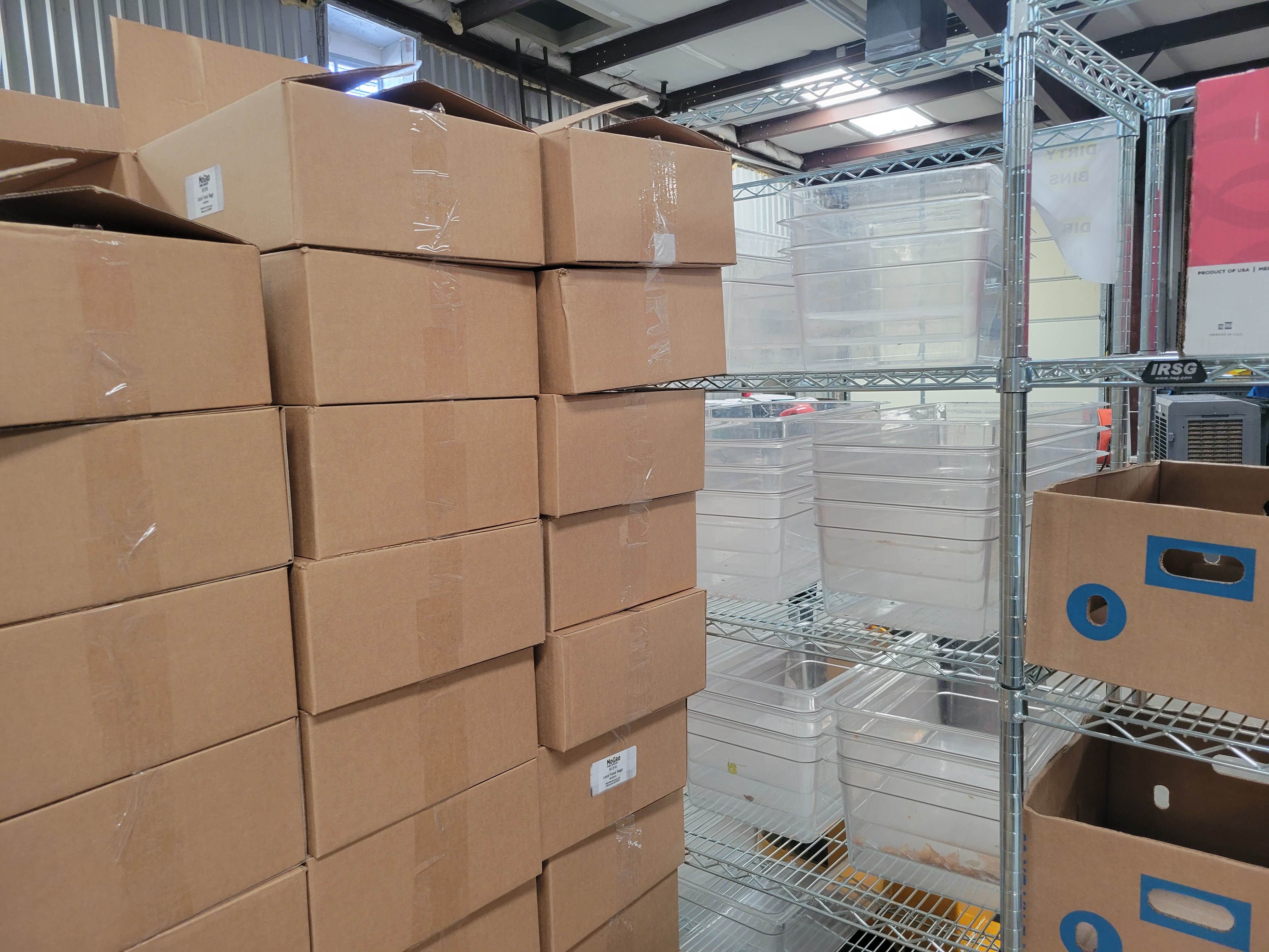 Smaller produce cardboard boxes on pallet next to various things filled shelves.