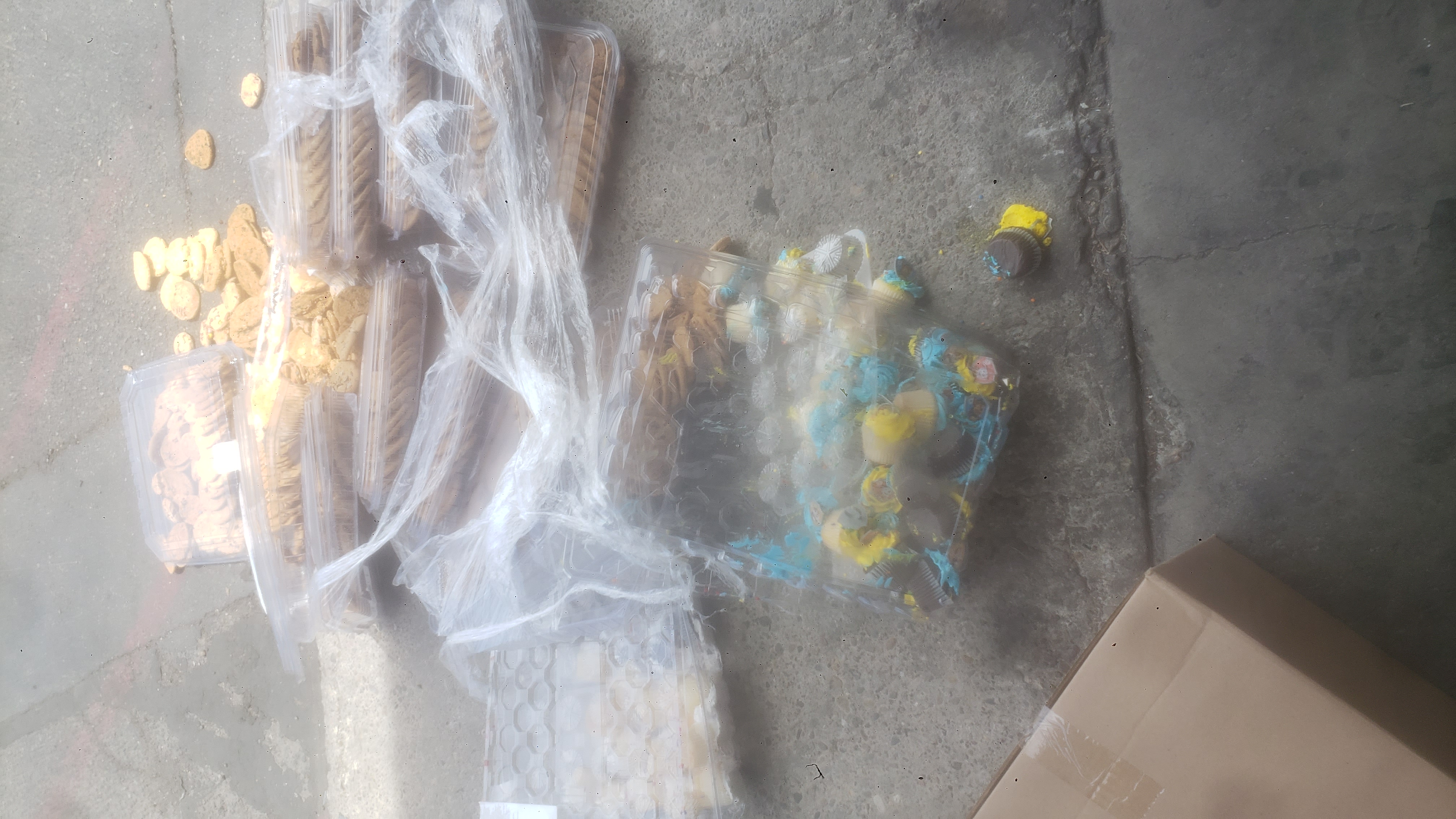 Containers wrapped in plastic with smashed cupcakes and cookies on a parking lot.