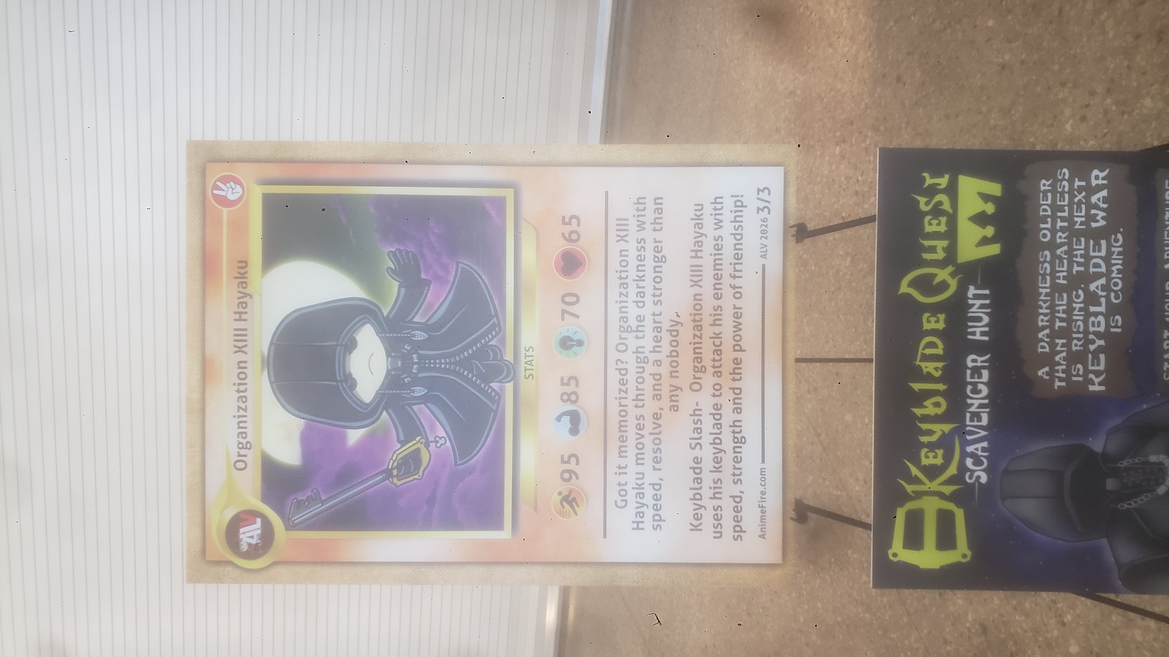 Sign designed like a Organization 13 hooded version of anime las vegas mascot trading card with another sign for a keyblade scavenger hunt.