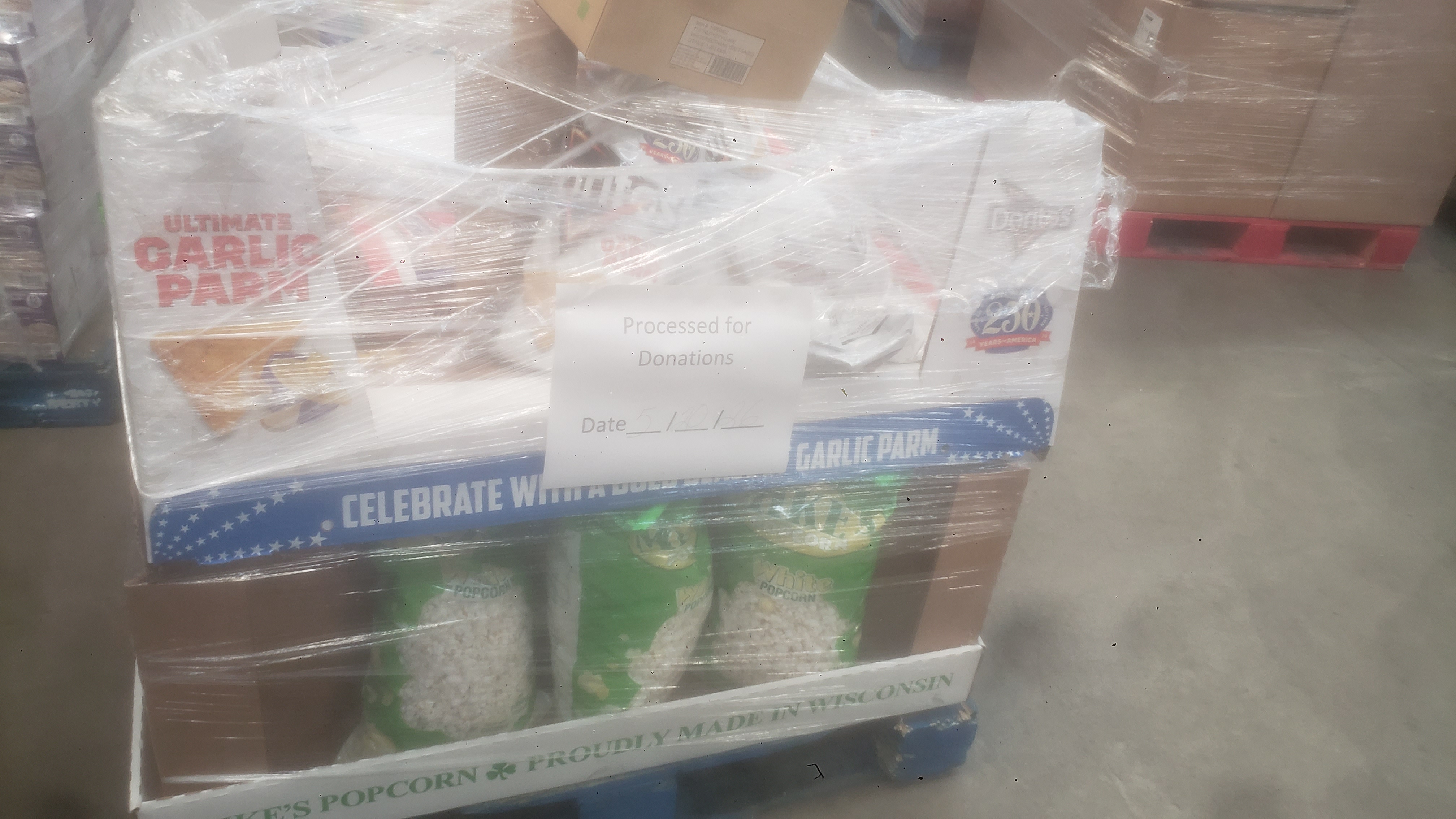 A pallet of garlic parmesan chips and white popcorn bags in cardboard trays wrapped in plastic and labeled reserved for donations.