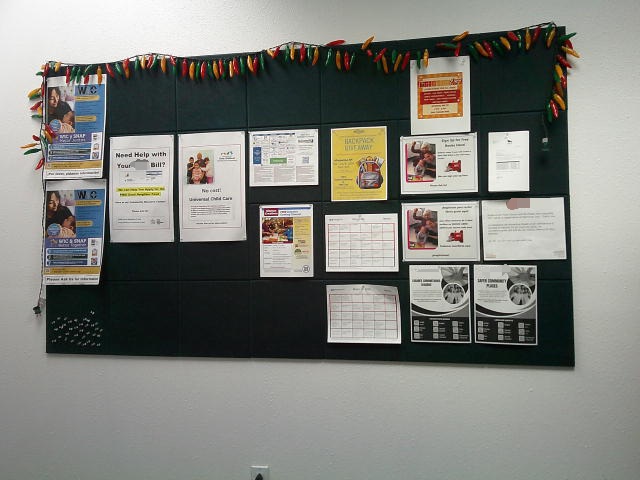 Community bulletin board with various flyers for resources decorated with plastic chili pepper lights.