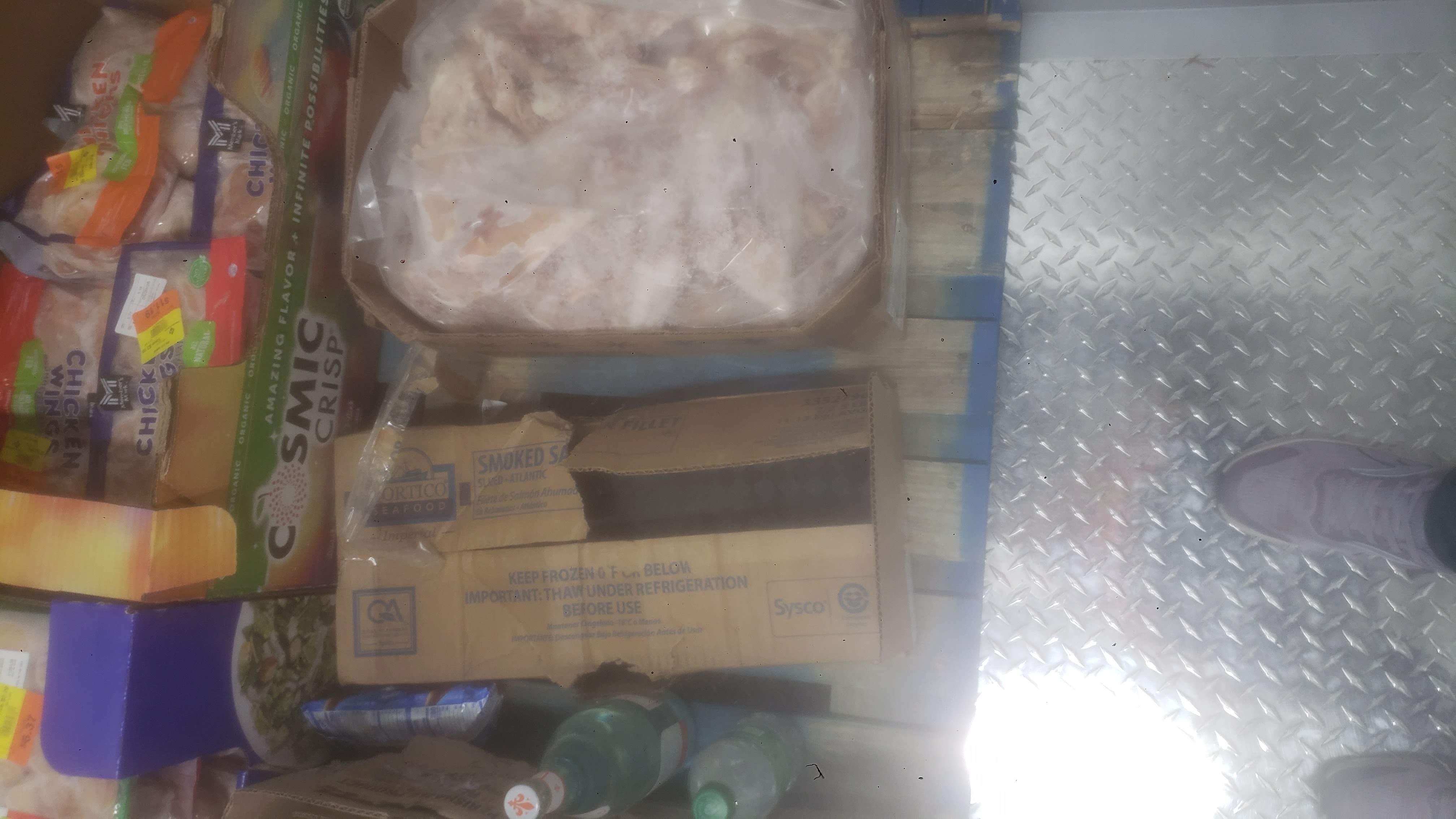 Bottle of water and sprite next to boxes and trays of various meats on a pallet.