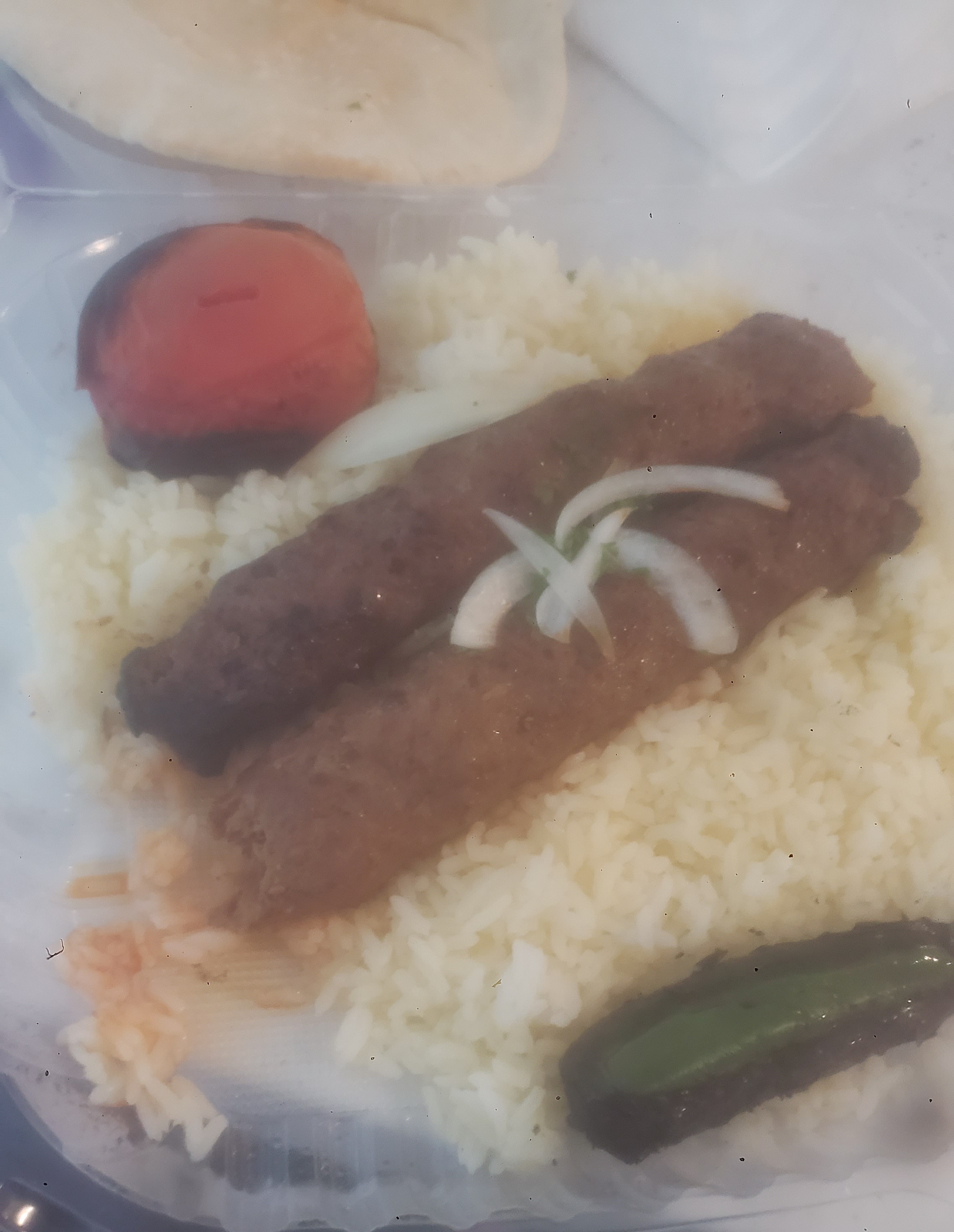 Kebab on a bed of rice next to a tomato and jalapeno.