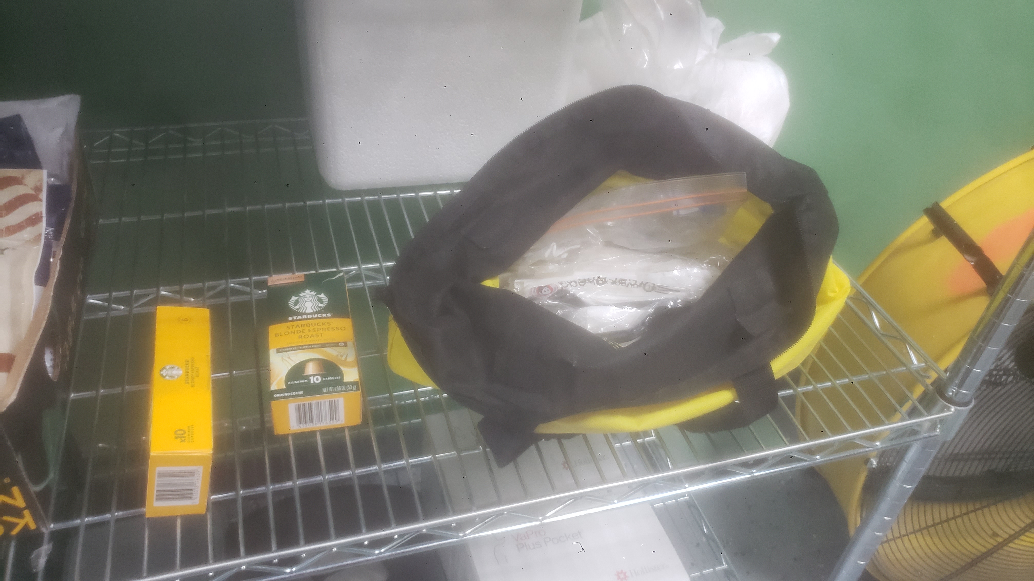 Starbucks blonde espresso roast coffee capsule box next to utility tote filled with plastic utensils on a shelf.