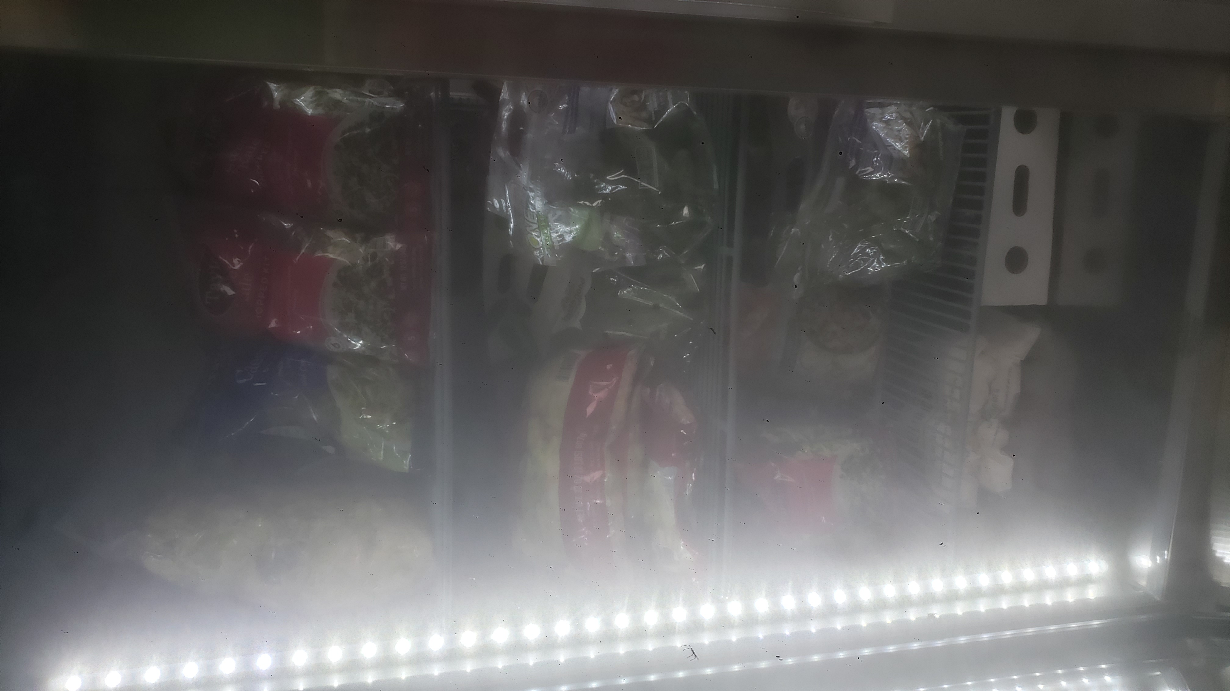 Bags of salad in a fridge.